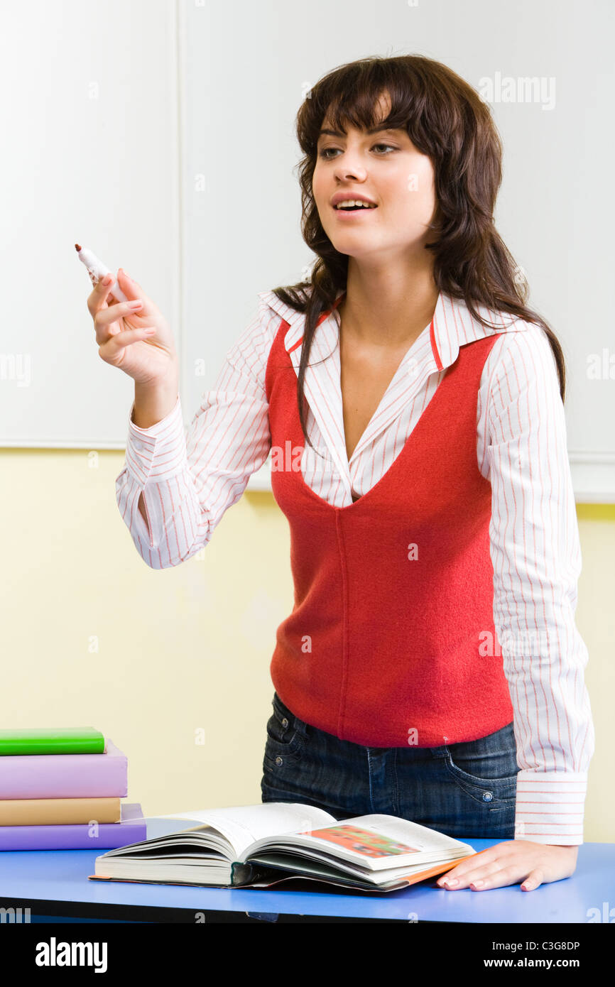 Portrait of confident teacher standing at her desk with open textbook ...