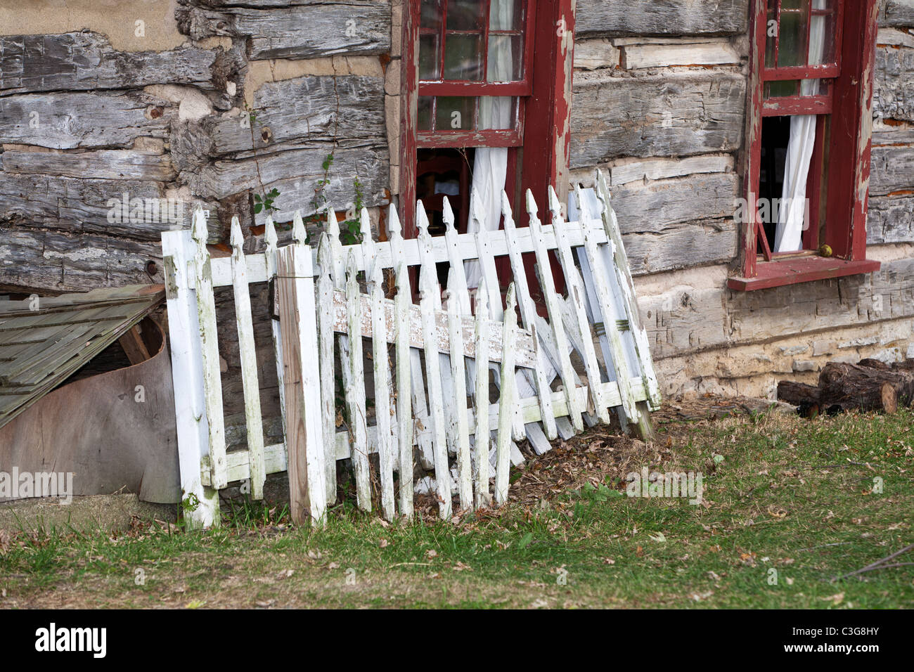 Old white picket fence leaning against an old cabin wall Stock Photo
