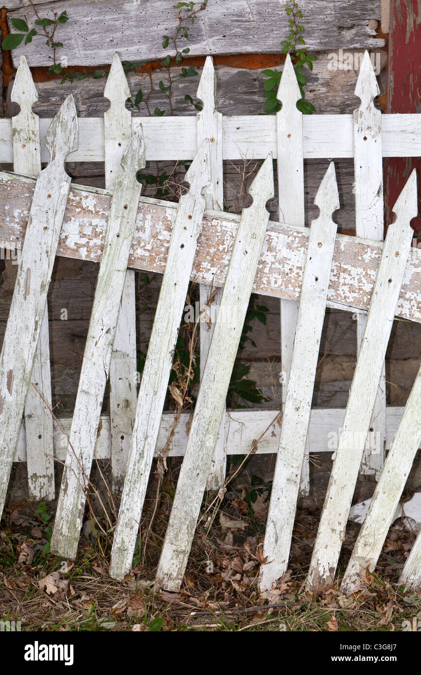 Old white picket fence leaning against an old cabin wall Stock Photo