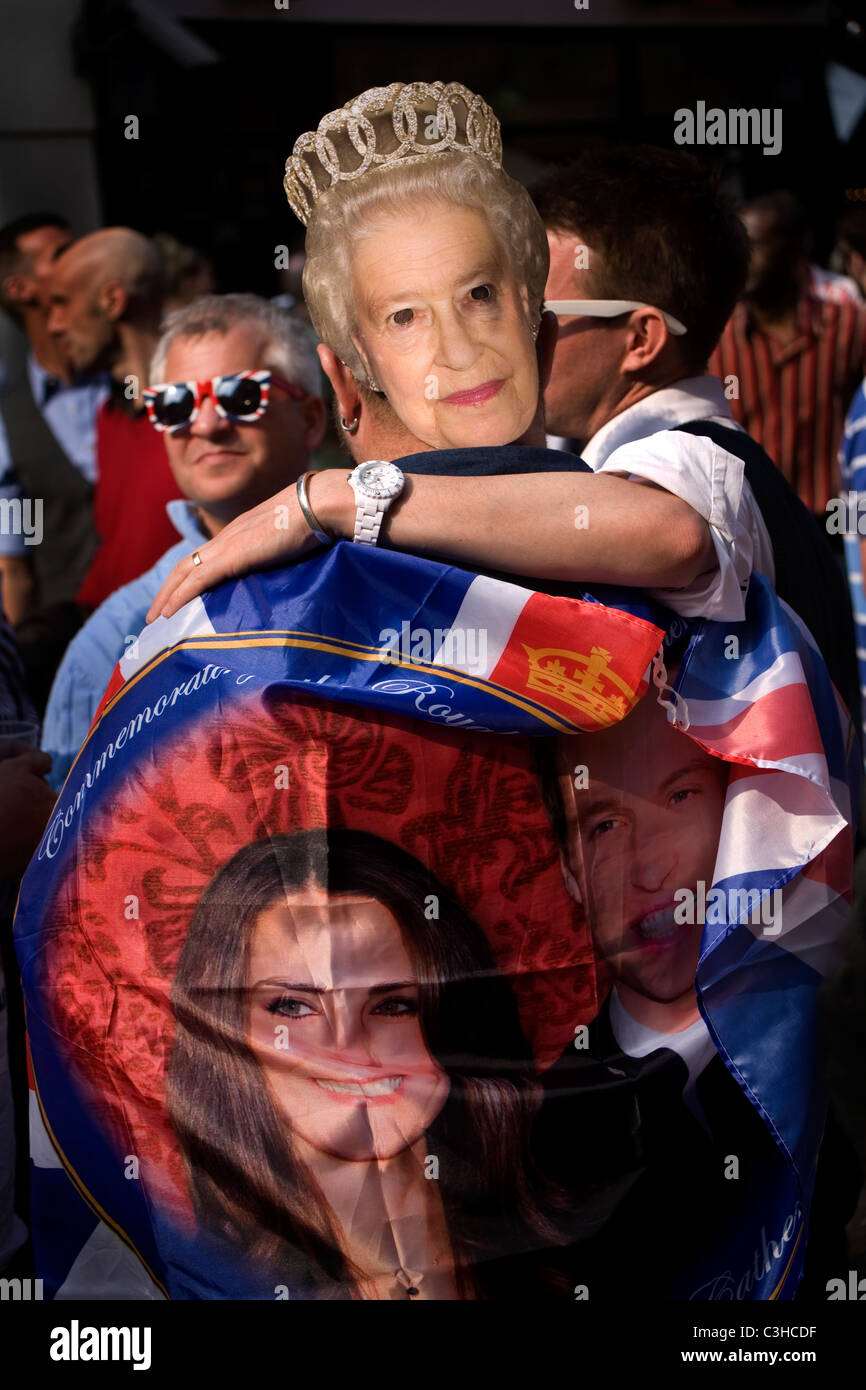 People wearing the mask of Queen Elisabeth and a flag of Prince William and Kate to celebrate their wedding, Soho, London. Stock Photo