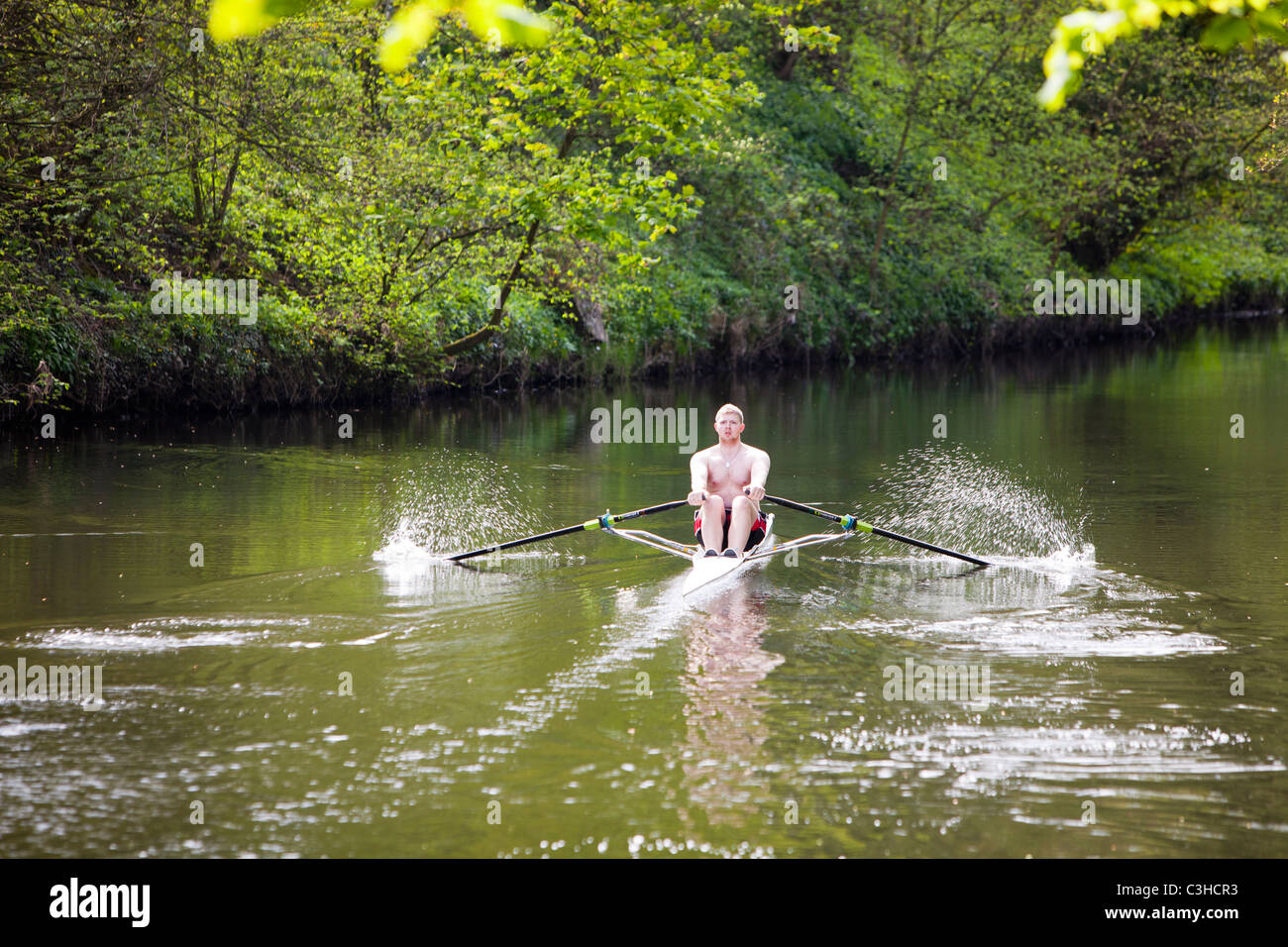 A man in a single skull rowing boat on the River Aire near Saltaire in Yorkshire, UK. Stock Photo