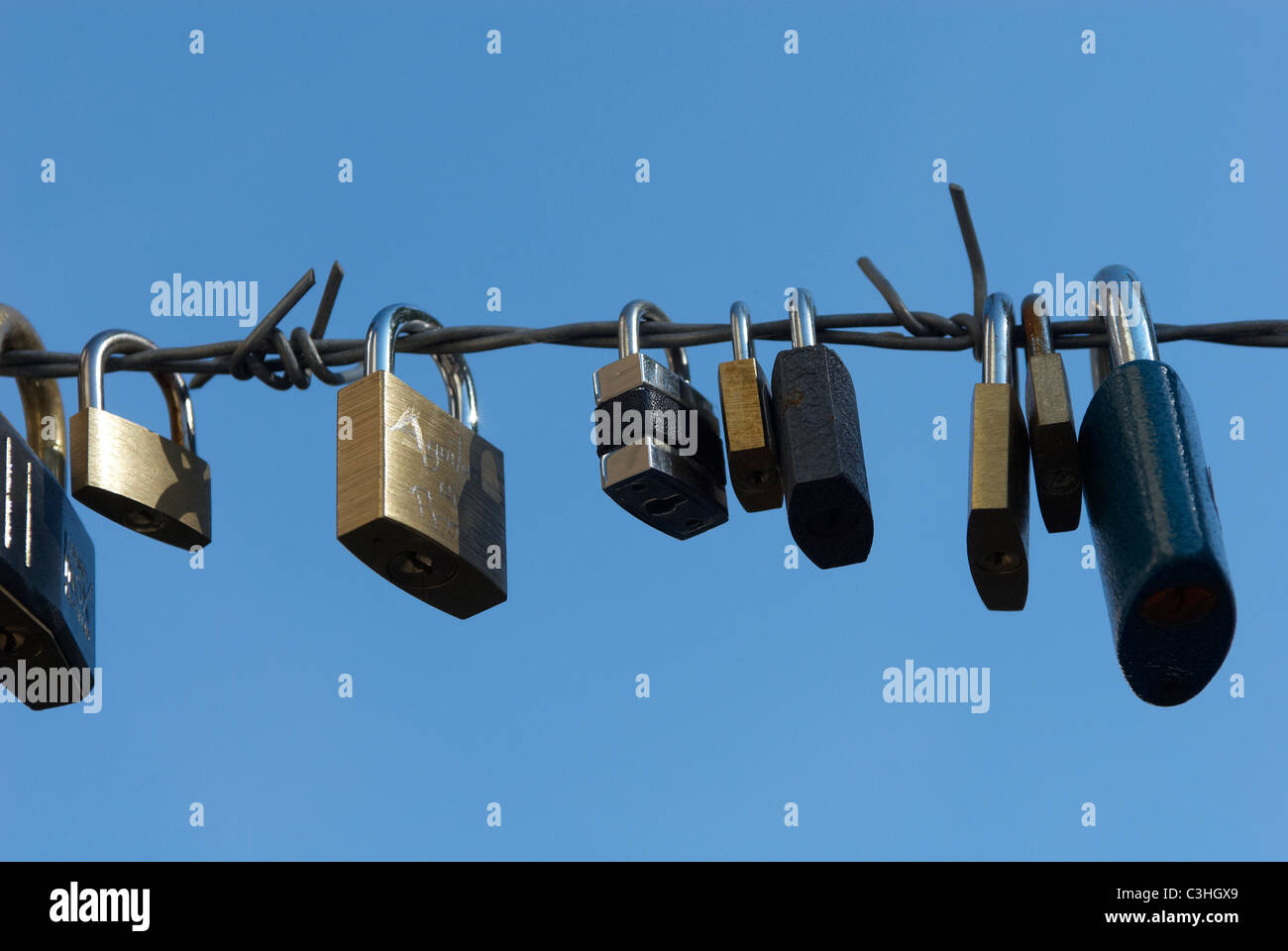 padlocks with heart shape attached to wire fence with blue sky background Stock Photo