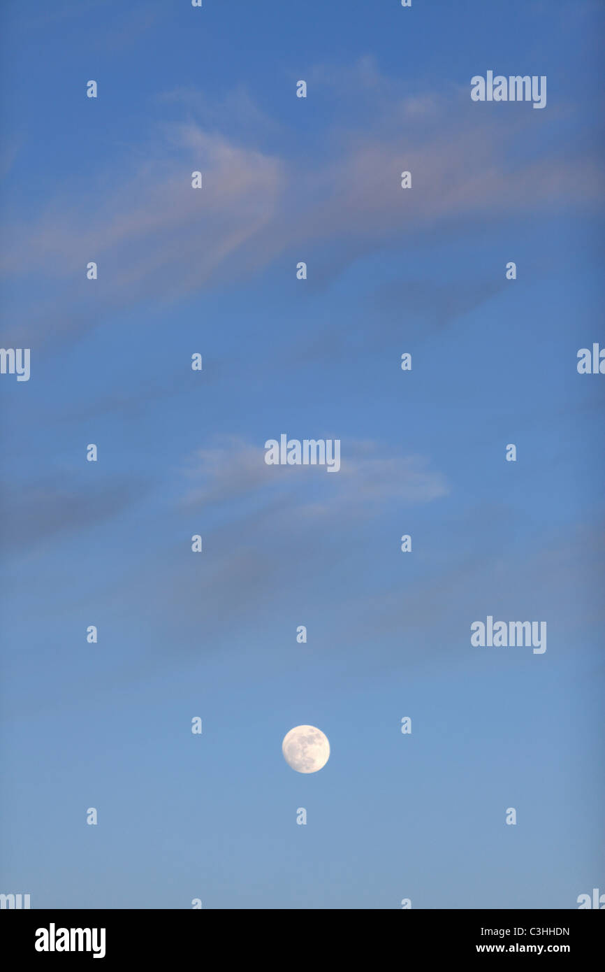 Full moon rises under a twilight sky and clouds Stock Photo
