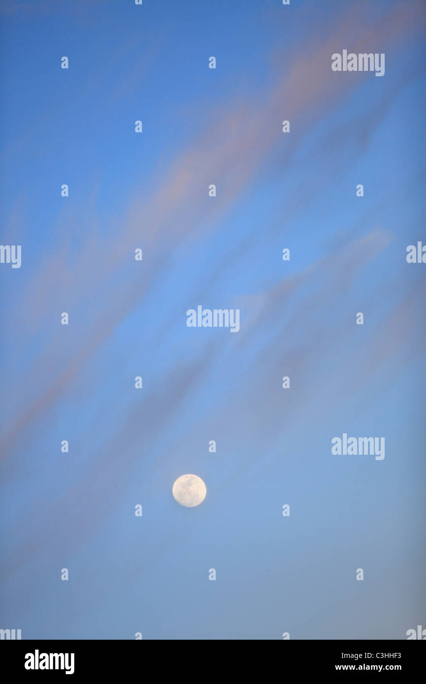 Full moon rises under a twilight sky and clouds Stock Photo