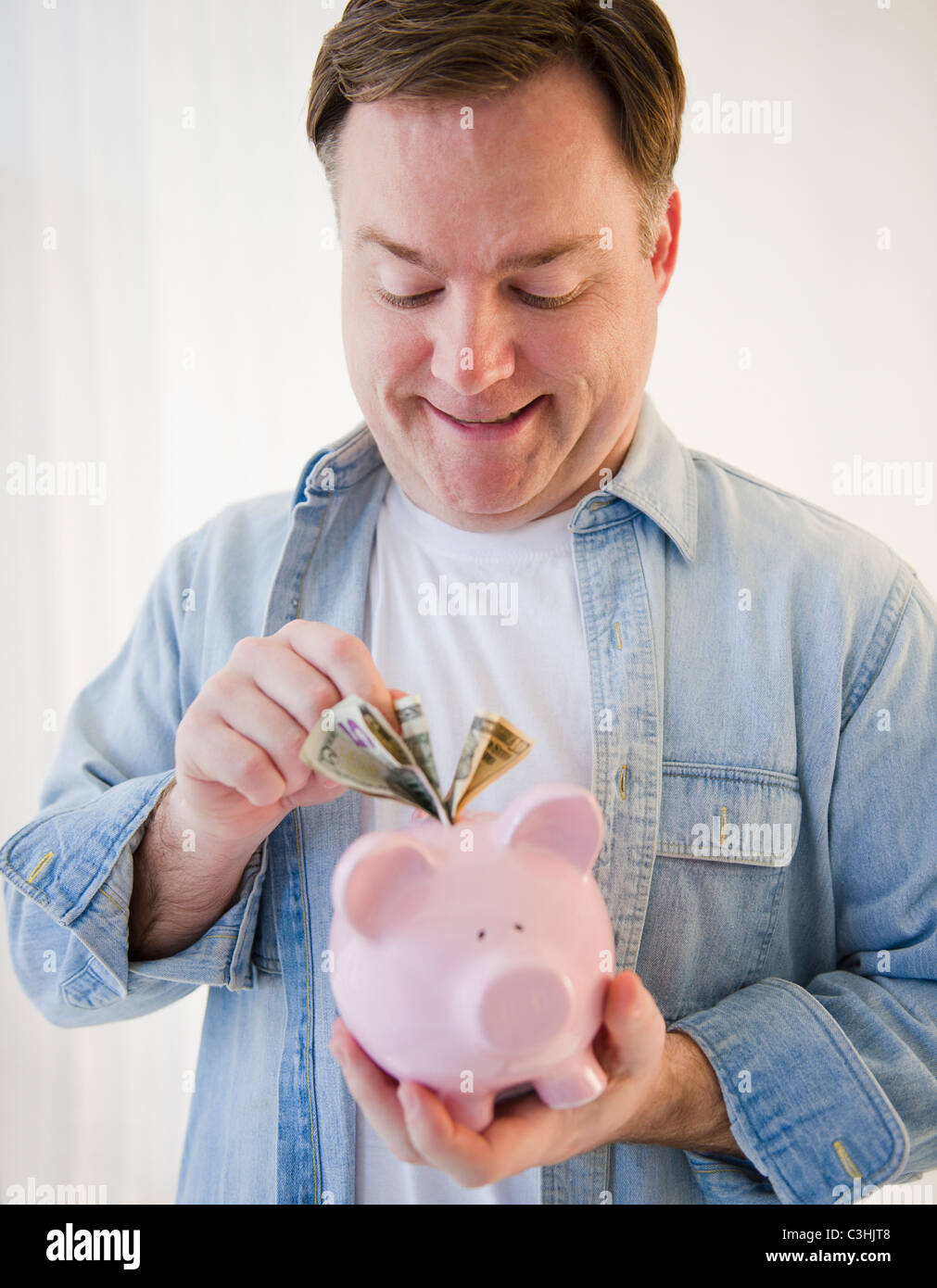 Man putting money into piggy bank Stock Photo - Alamy