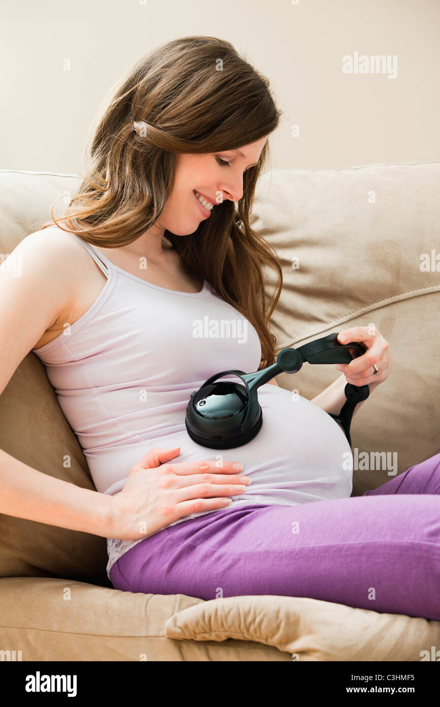 Young pregnant woman playing music through headphone to ...