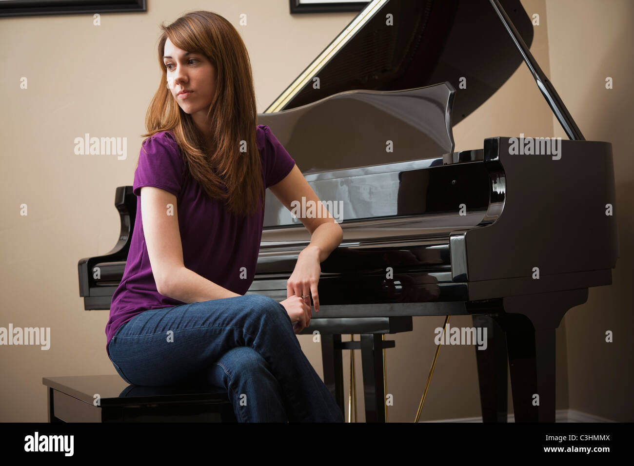 Young woman sitting by grand piano Stock Photo