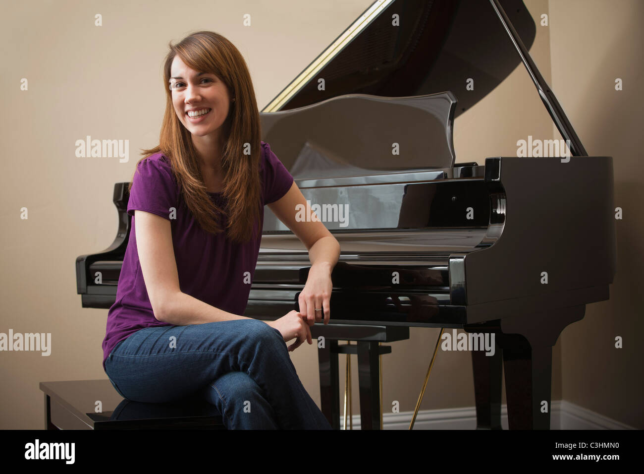 Young woman sitting by grand piano, smiling Stock Photo