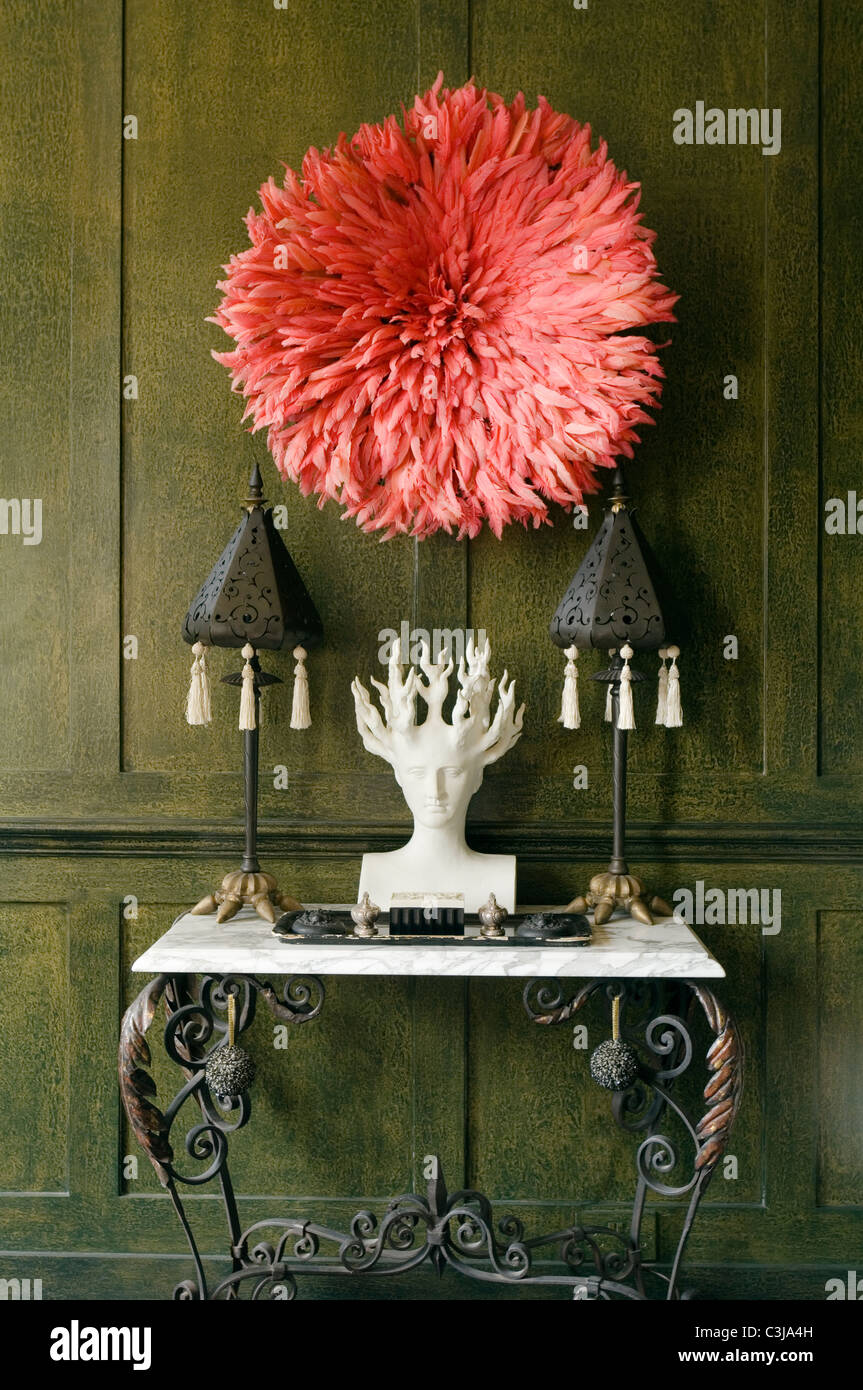 Medusa bust on marble top console table against green panelled wall with red feather hat above Stock Photo