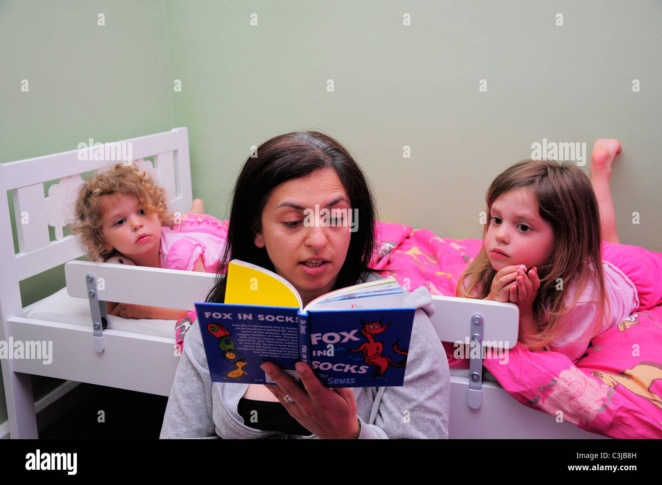 Mother reading a Dr Suess childrens story to her daughters at bedtime. Stock Photo