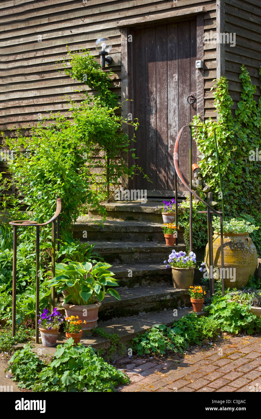stone steps with metal handrail winding up stairway outside barn edged with pots in english garden Stock Photo