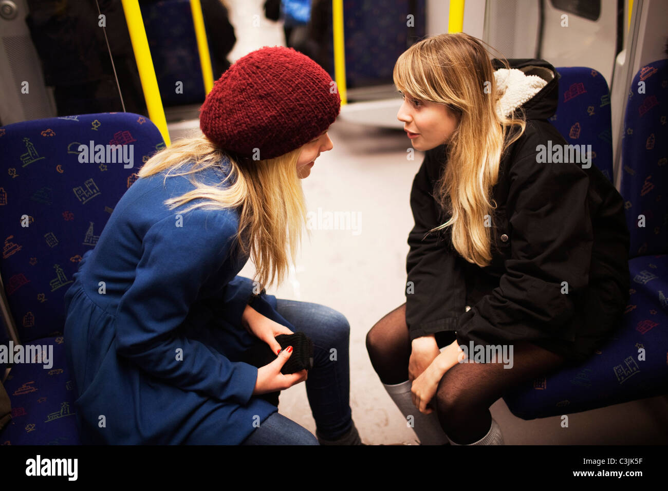 Two teenage girls talking on subway train Stock Photo