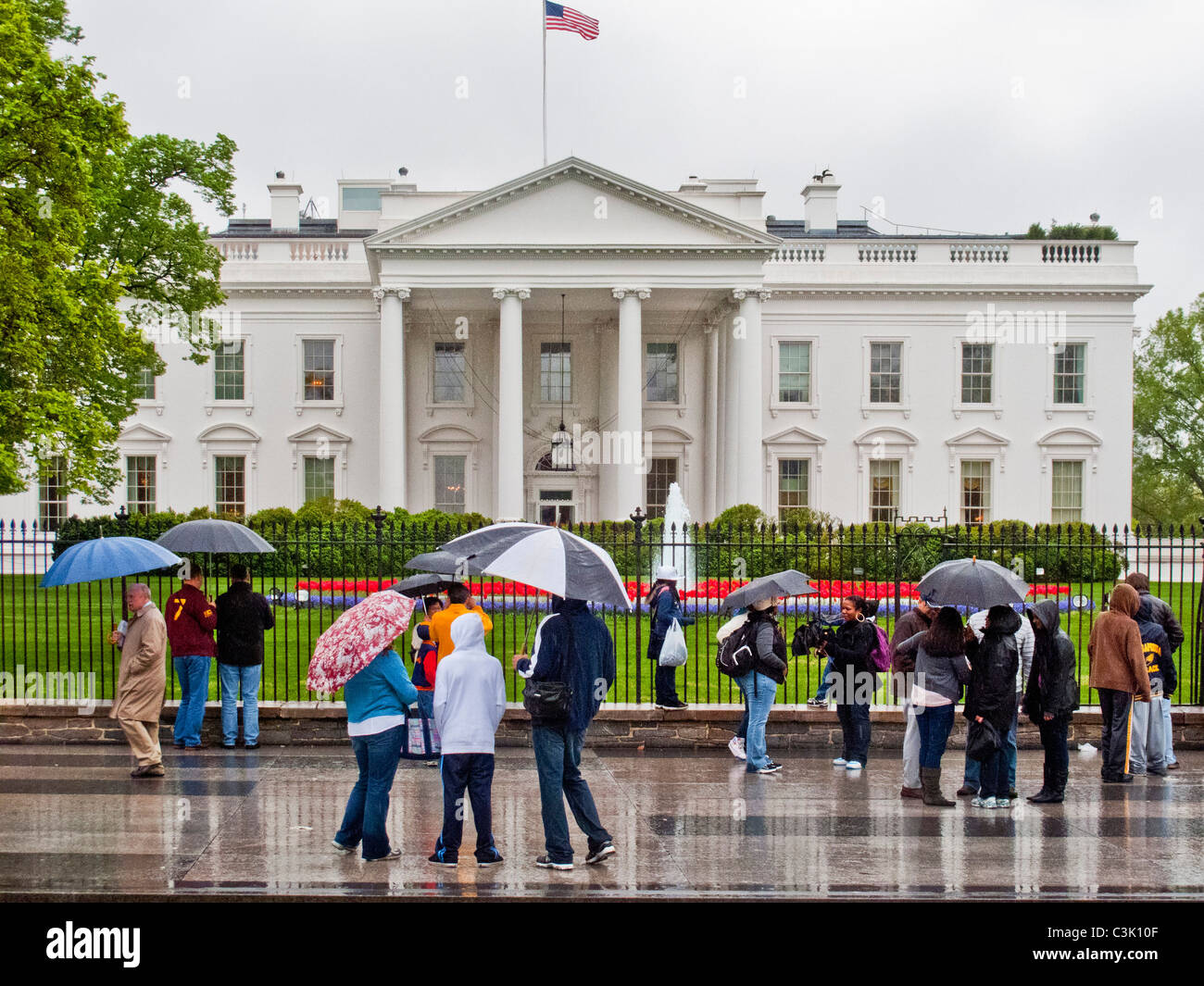 Wearing raincoats and carrying umbrellas, tourists gather outside the White House in Washington, D.C. Stock Photo