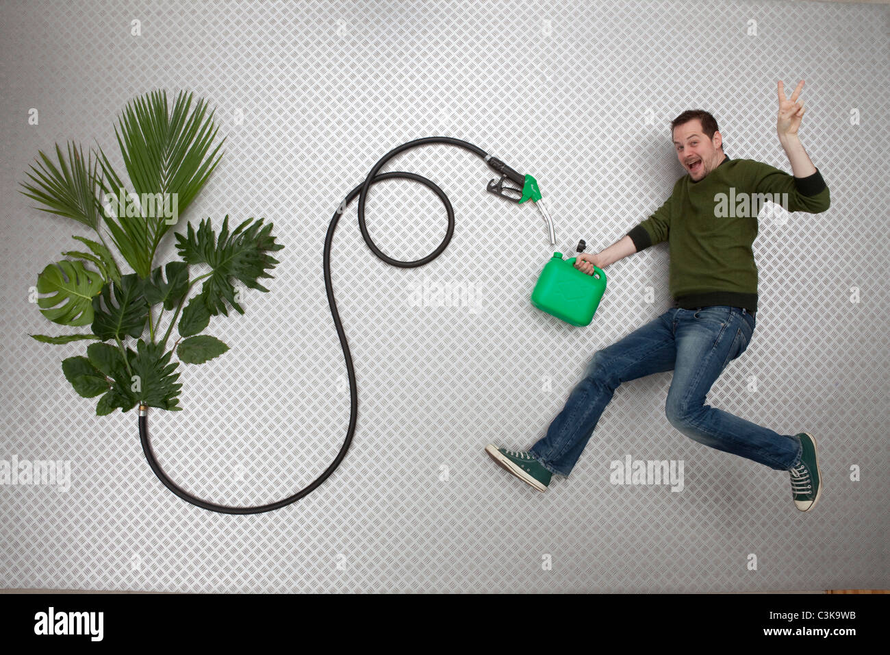 Mid adult man holding petrol can and hose connected to plant Stock Photo