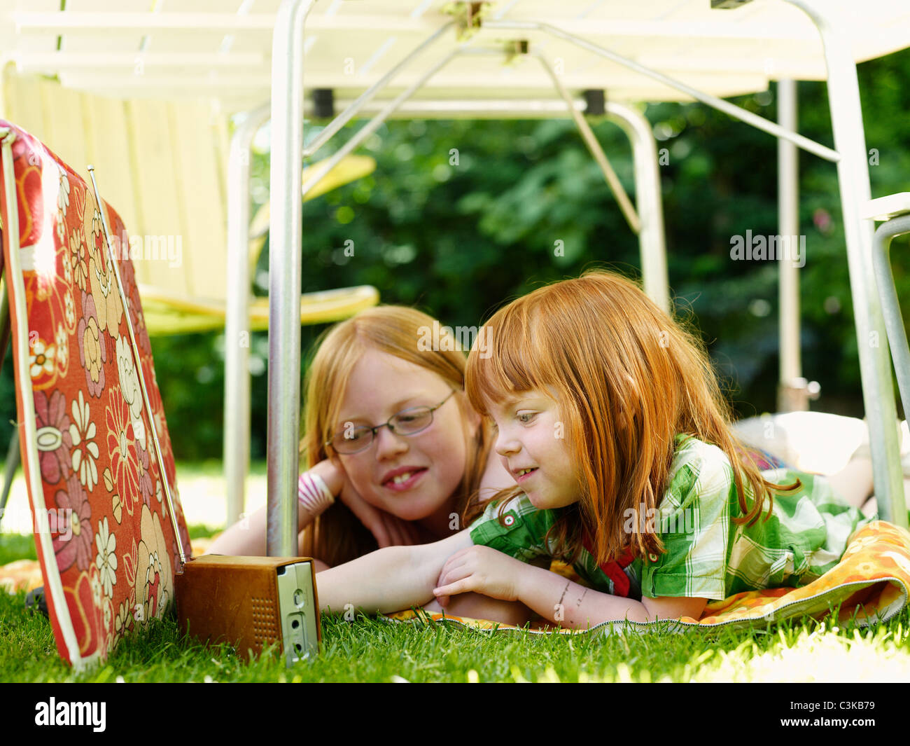 Two girls lying under outdoor table and listening to the radio Stock Photo
