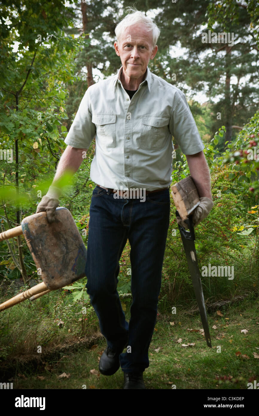 Senior man walking with holding saw and stool Stock Photo