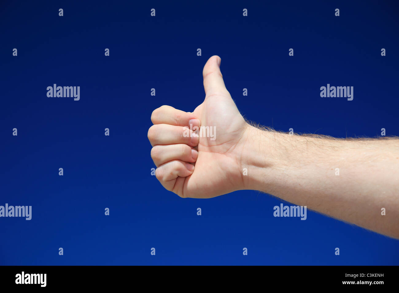 A persons hand making thumbs up sign in front of bright blue sky. Stock Photo
