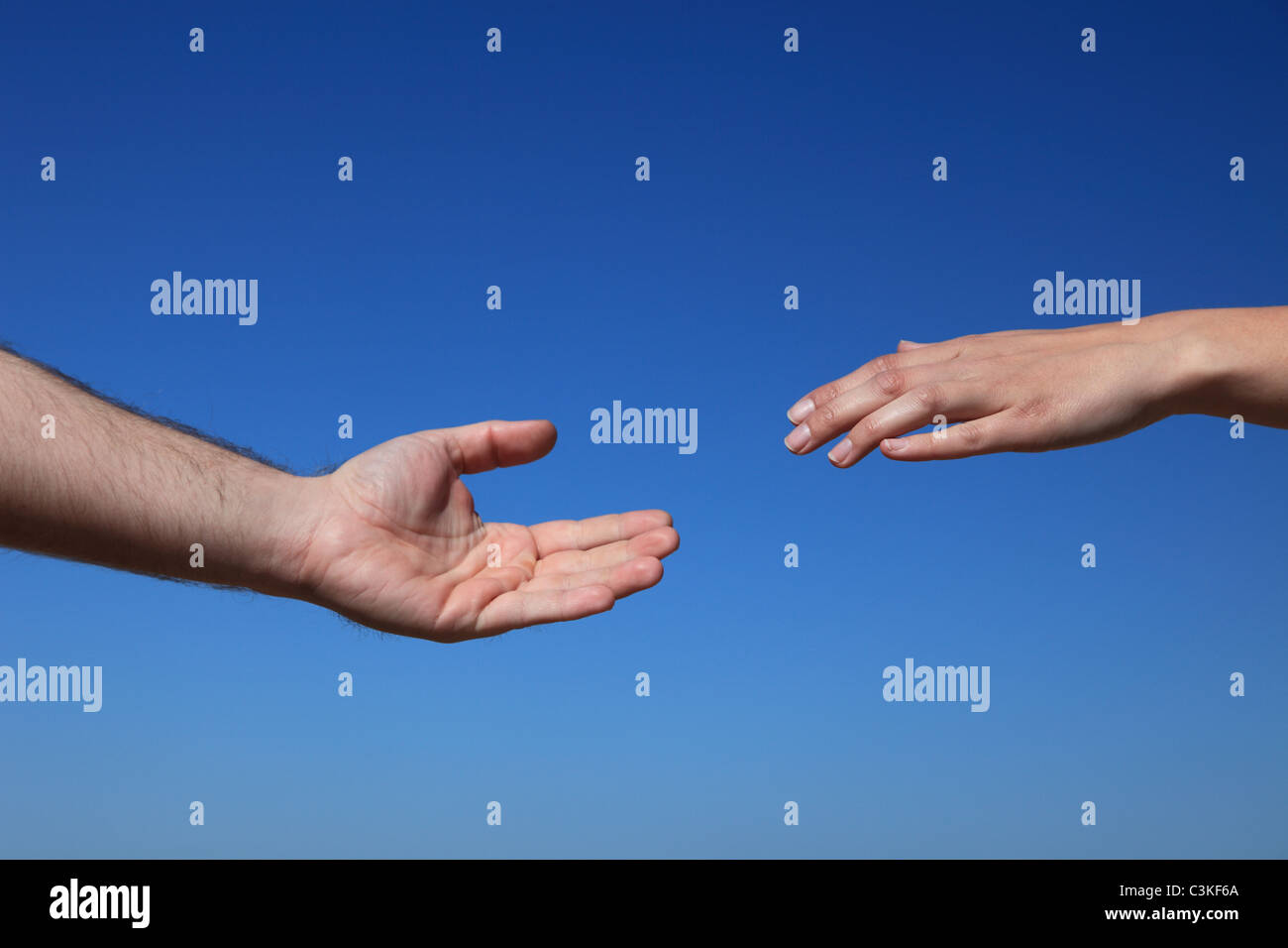 Two persons hands reach for each other in front of bright blue sky. Stock Photo