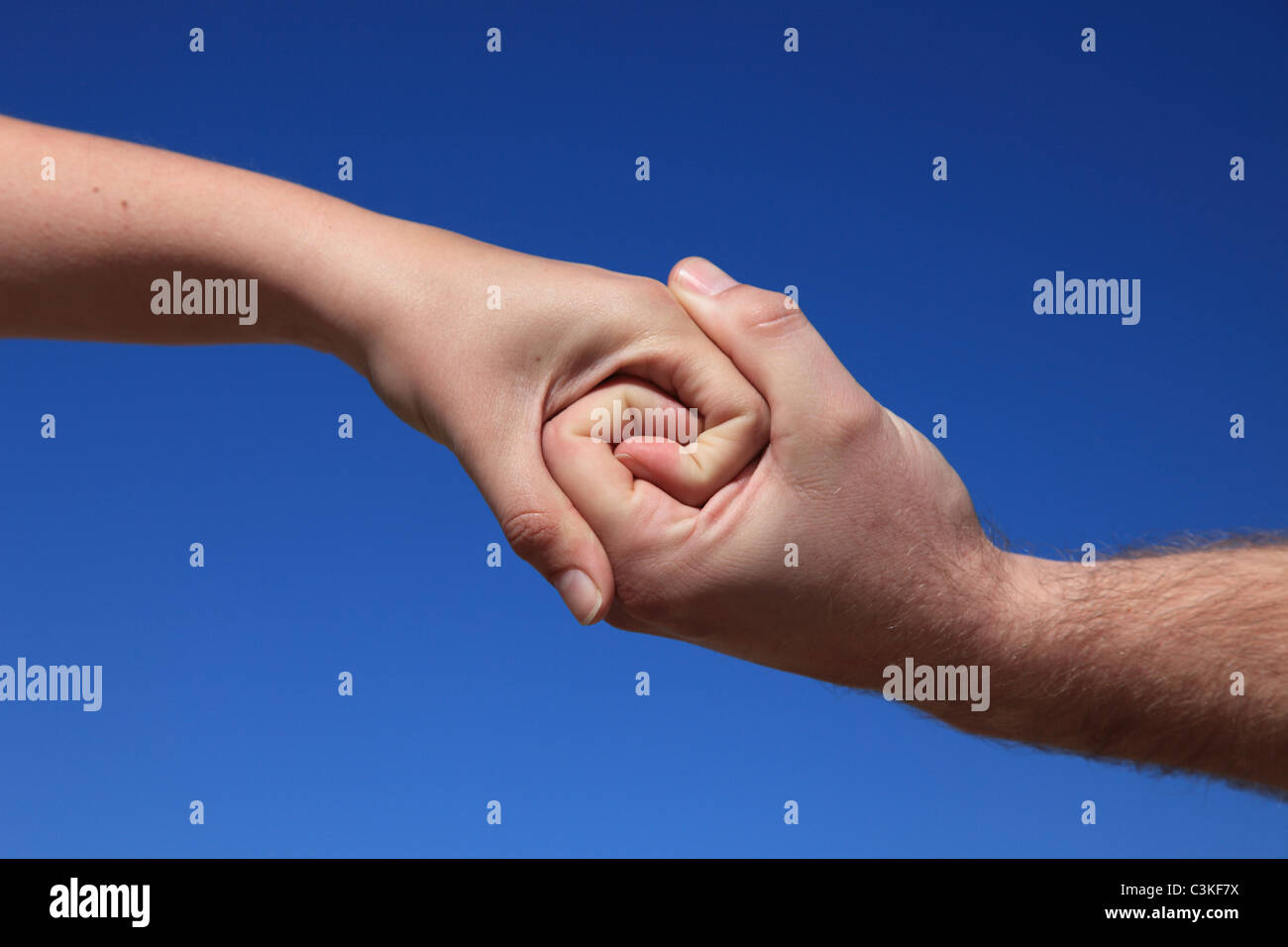 Two persons holding hands in front of bright blue sky. Stock Photo