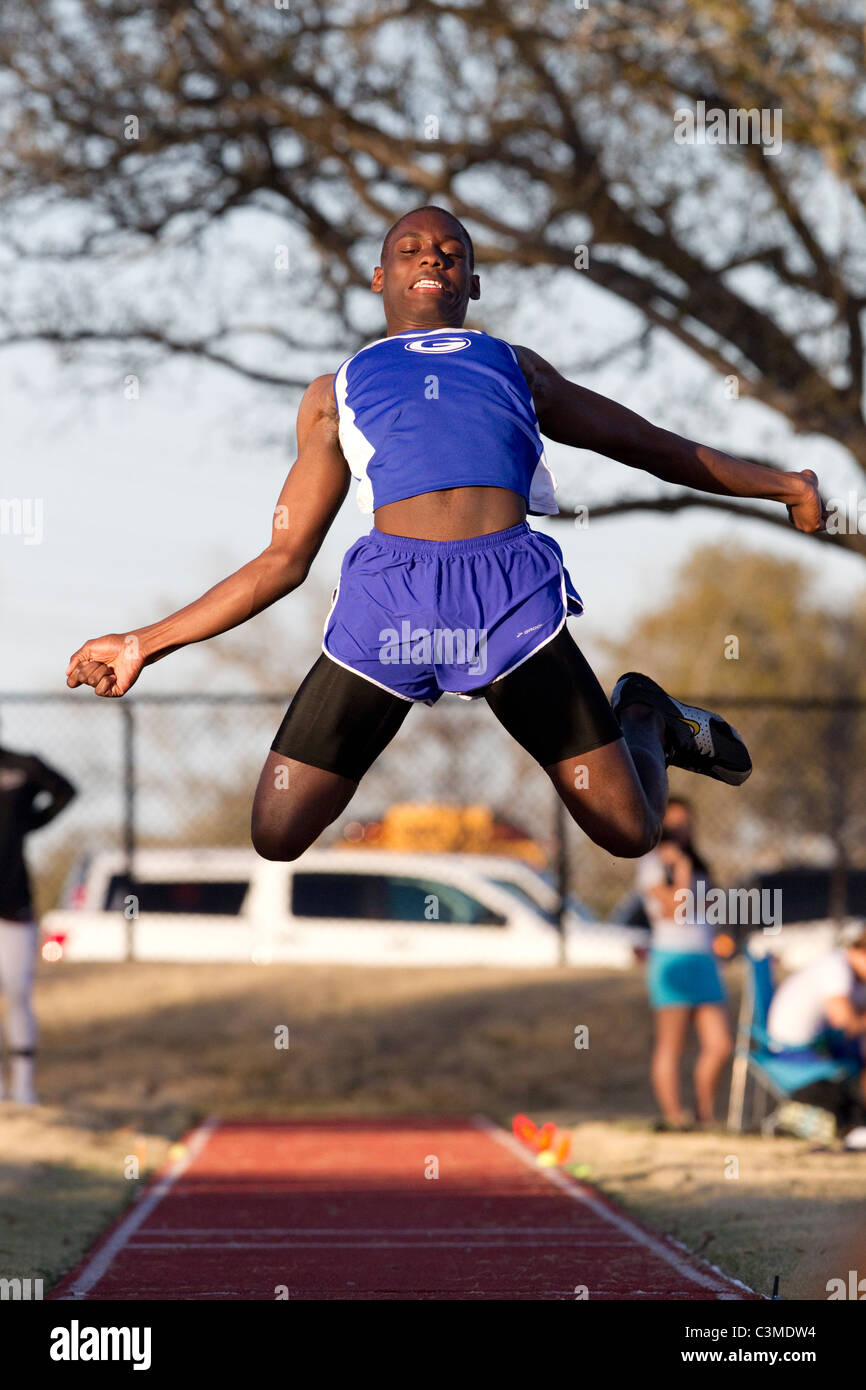 African-American male athlete leaps after takeoff in the long jump at high school track meet in San Antonio Texas Stock Photo