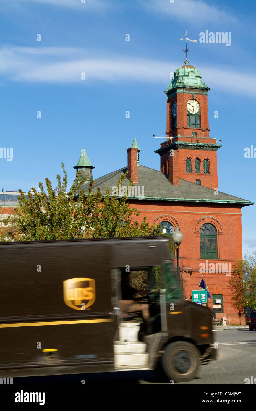 UPS tuck making a package delivery in Claremont, NH with Opera House in spring sun. Stock Photo