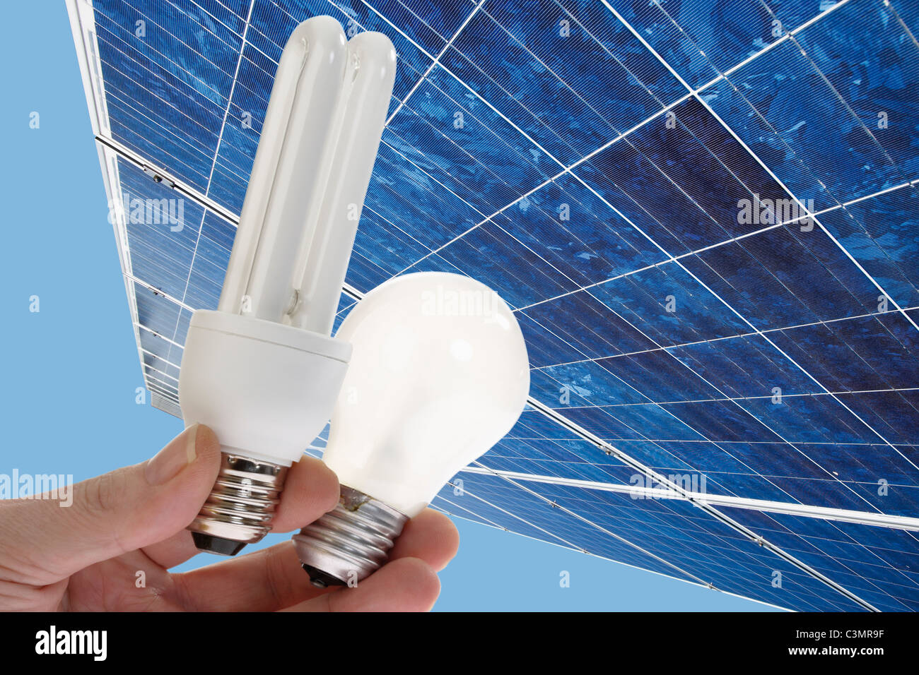 Human hand holding energy saving light, bulb against  solar panel, close up. Stock Photo