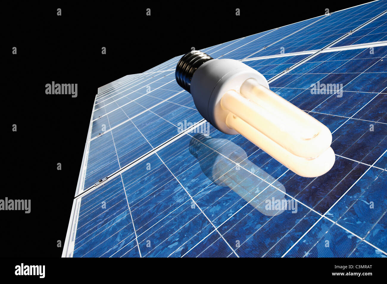 Energy saving lamp on solar panel against black background. Stock Photo