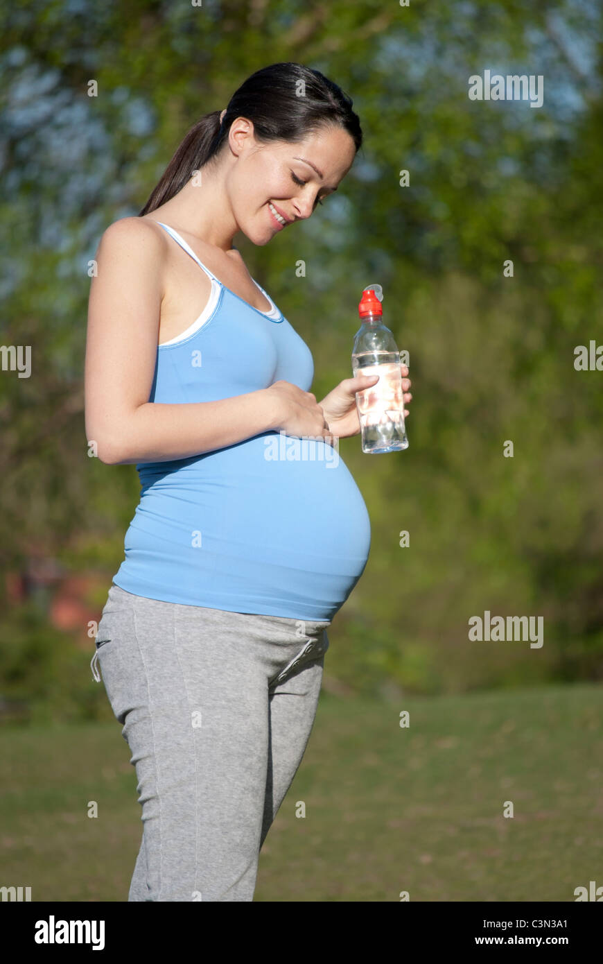 Pregnant woman looking at her bump holding bottle of water Stock Photo