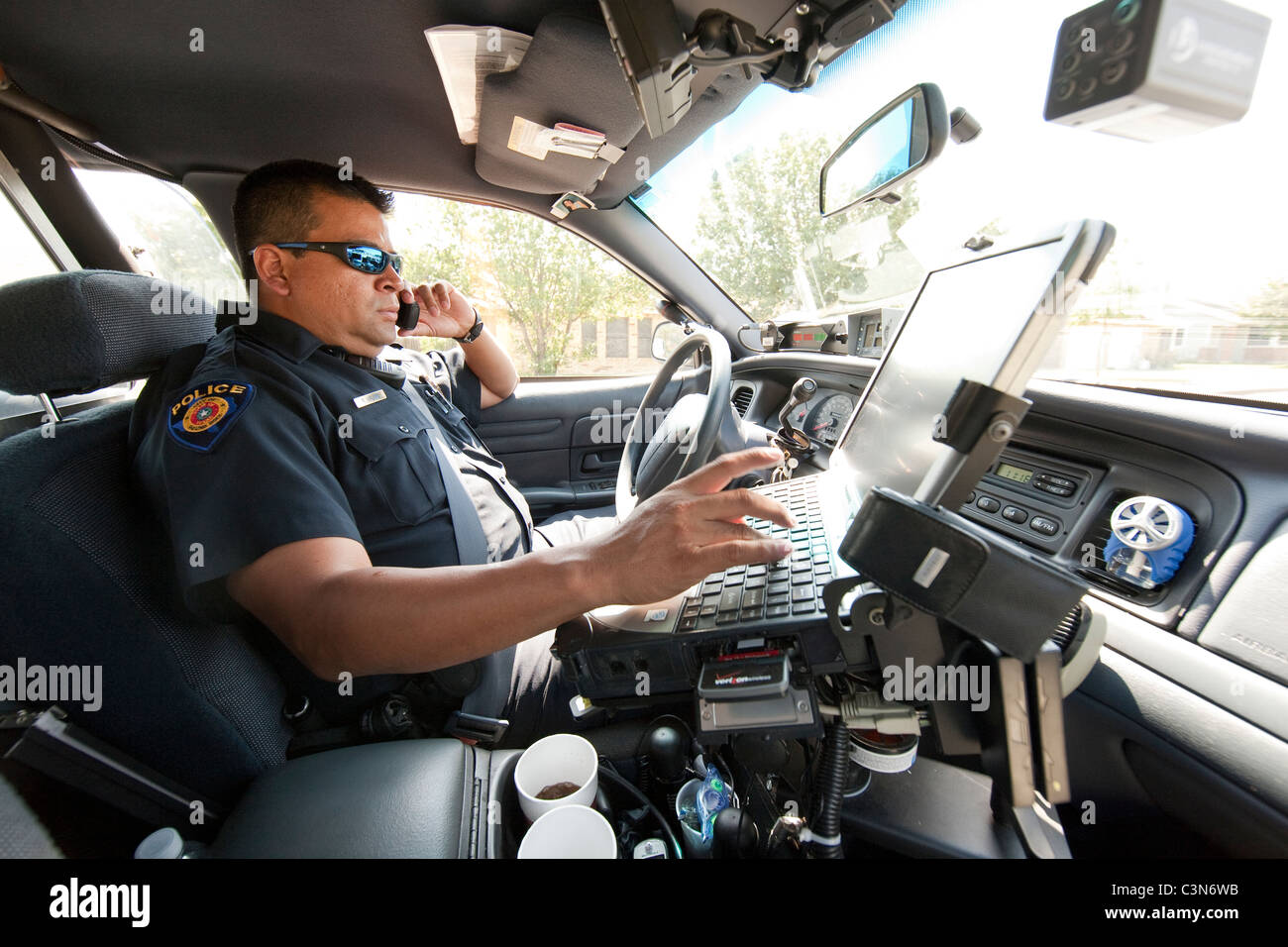 Hispanic Texas police officer talks on phone and types information into patrol car computer in Round Rock, Texas Stock Photo