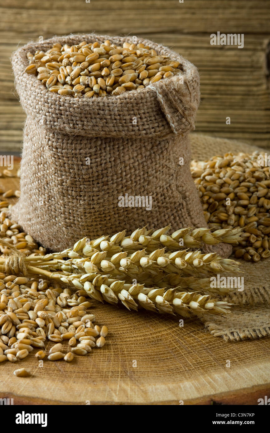 Wheat in small burlap bag on wooden background Stock Photo