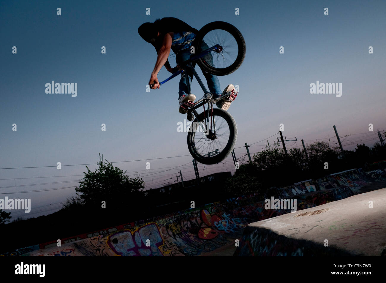 Young BMX rider performing a jumping trick against sunset, London 2011