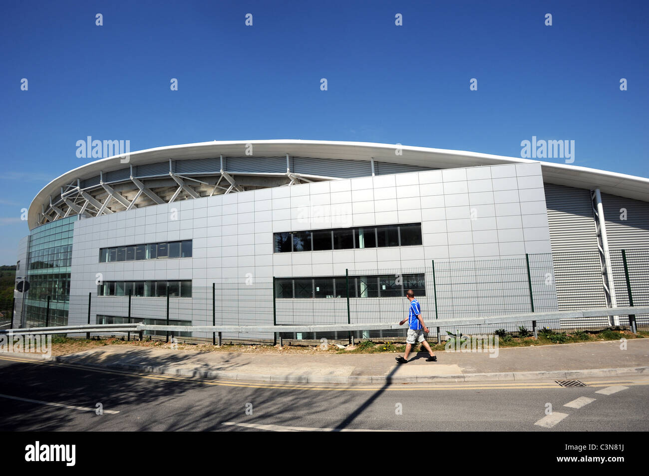 A fan walks past the Brighton and Hove Albion's new Football Stadium called the American Express Community Stadium or The Amex Stock Photo