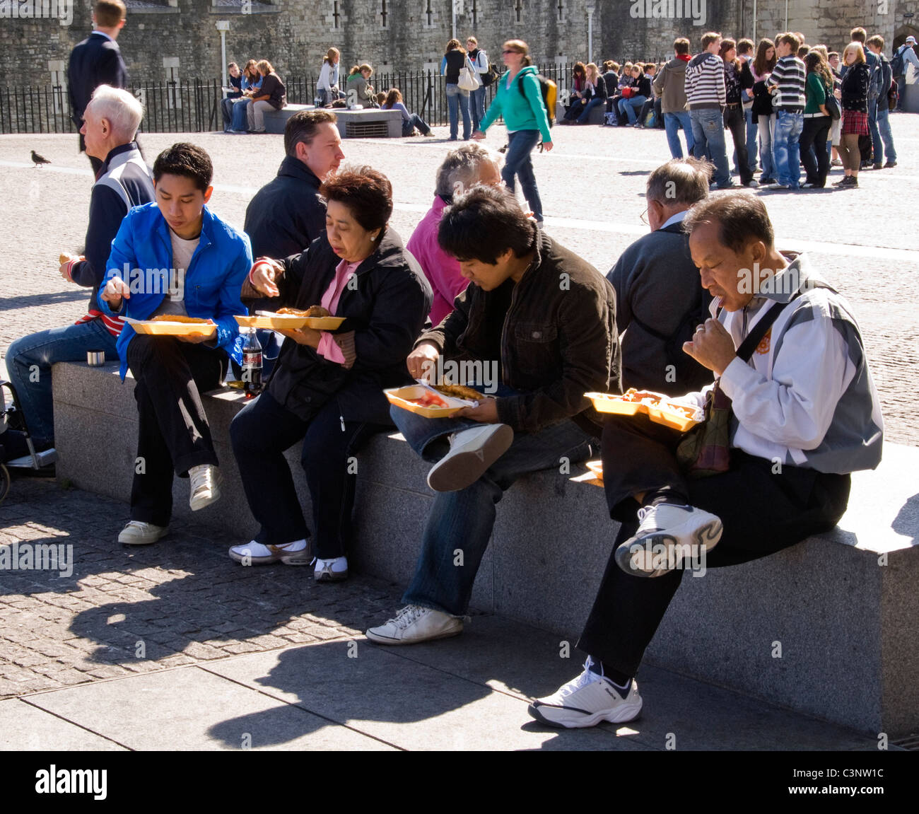 Asian tourists eating takeaway food at the Tower of London, London