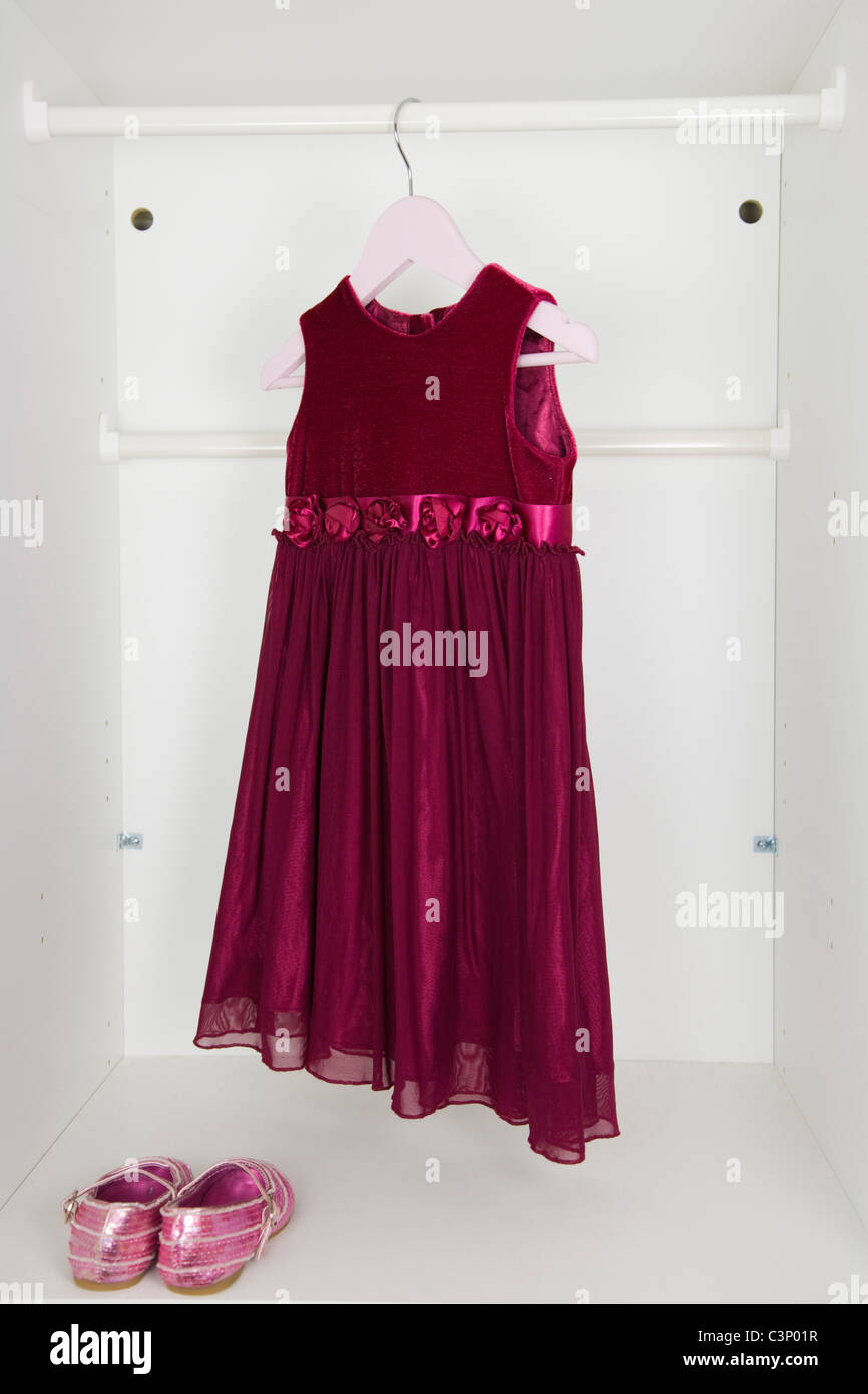 Small girl's wine red party dress and pink sequin shoes in the white wardrobe. Stock Photo
