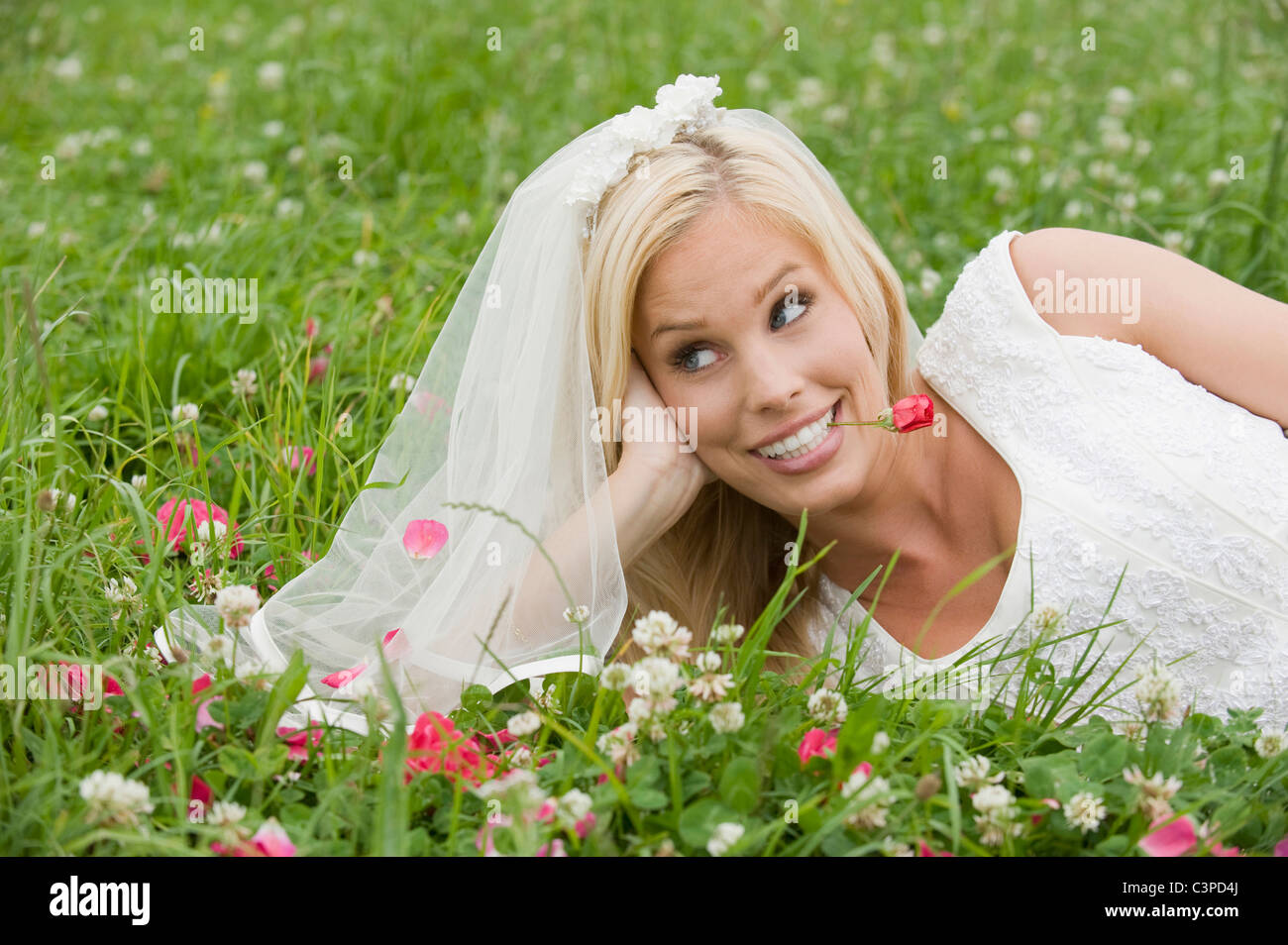 Bride lying on meadow, smiling, looking away. Stock Photo