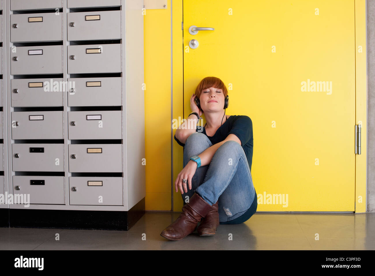 Germany, Leipzig, Young woman sitting and listening music in locker room Stock Photo