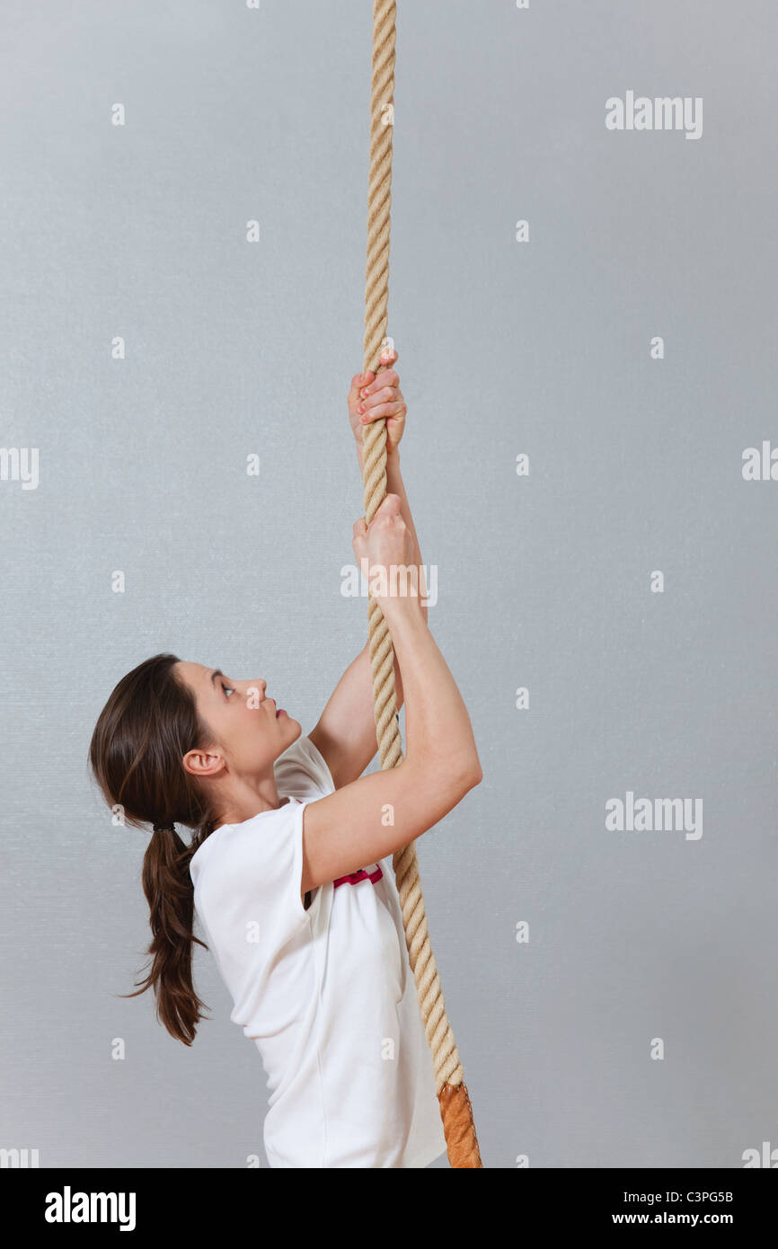 Germany, Berlin, Young woman climbing rope in school gym Stock