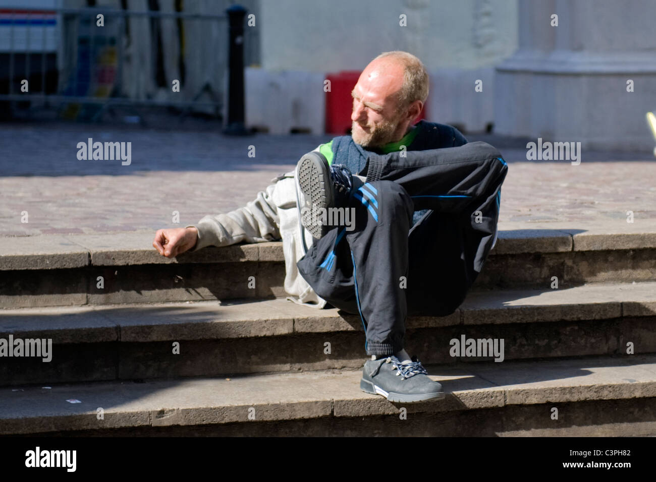 Young balding scruffy man sitting on steps of Charing Cross Station , bearded homeless vagrant tramp hobo tourist ? Stock Photo