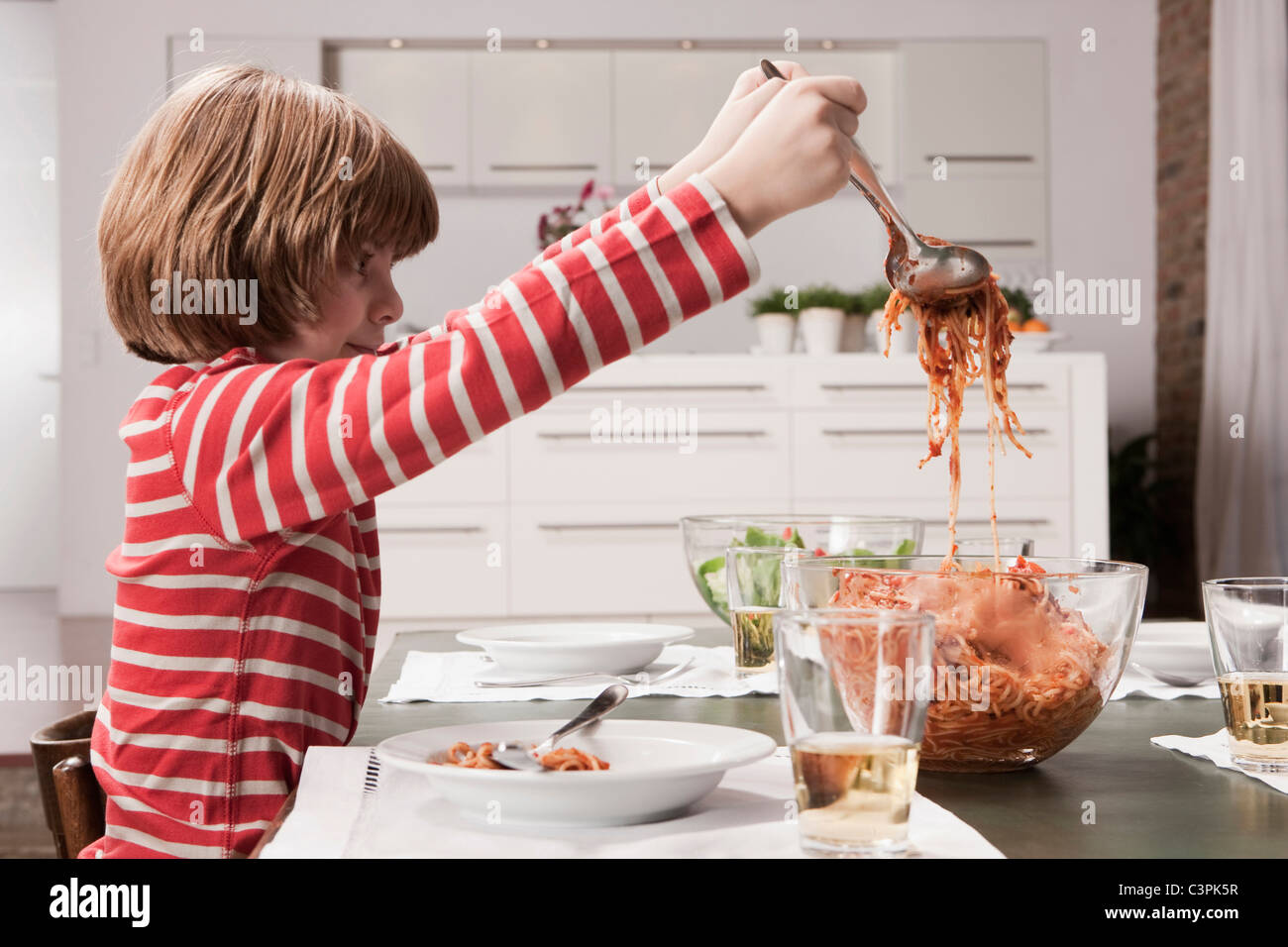Germany, Cologne, Boy (6-7) serving spaghetti, side view Stock Photo