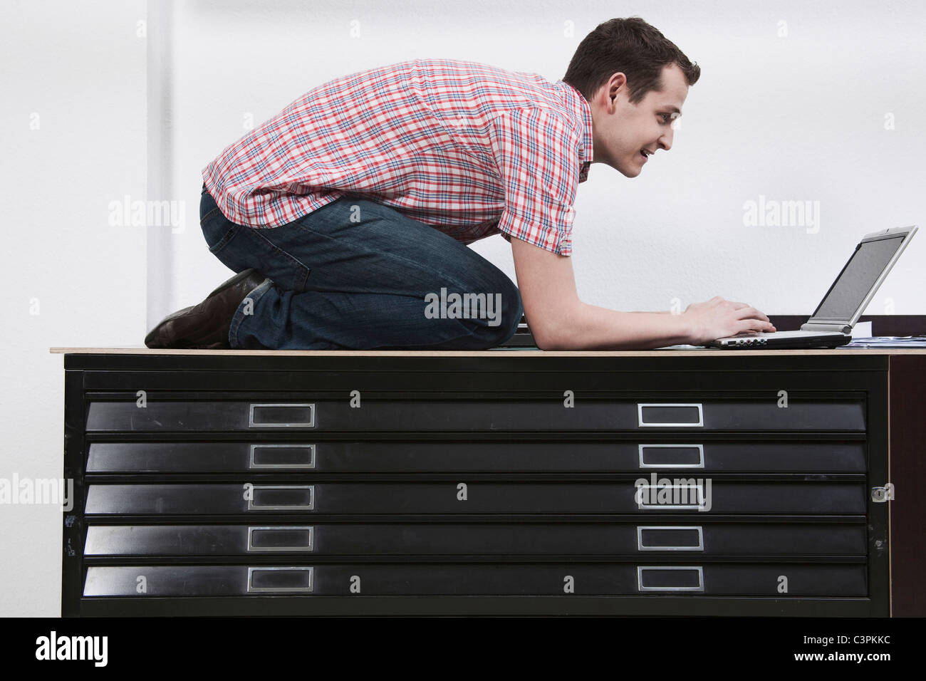 Man kneeling on desk using laptop Stock Photo Alamy