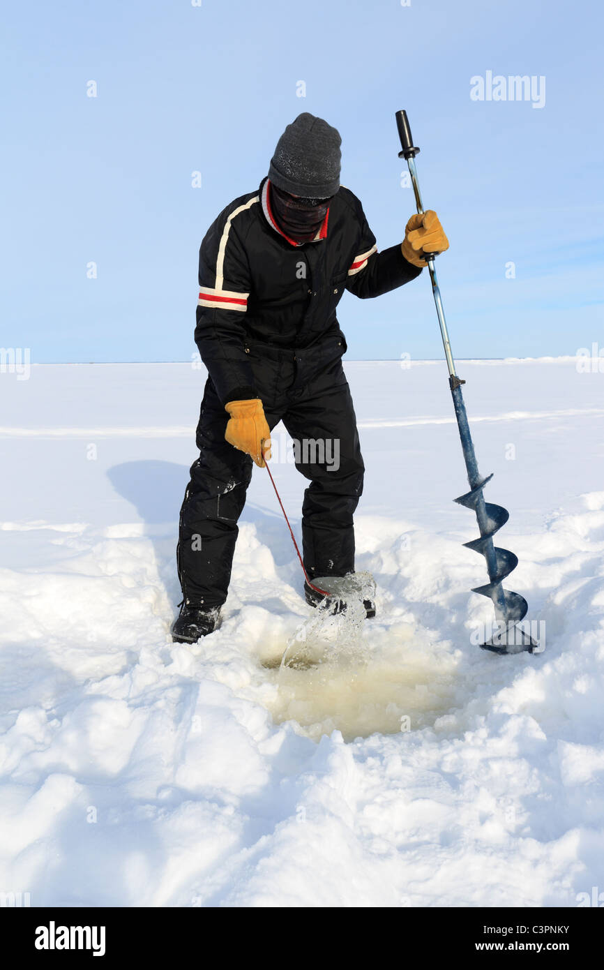 An ice fisherman uses a skimmer to clear a just-opened hole on a