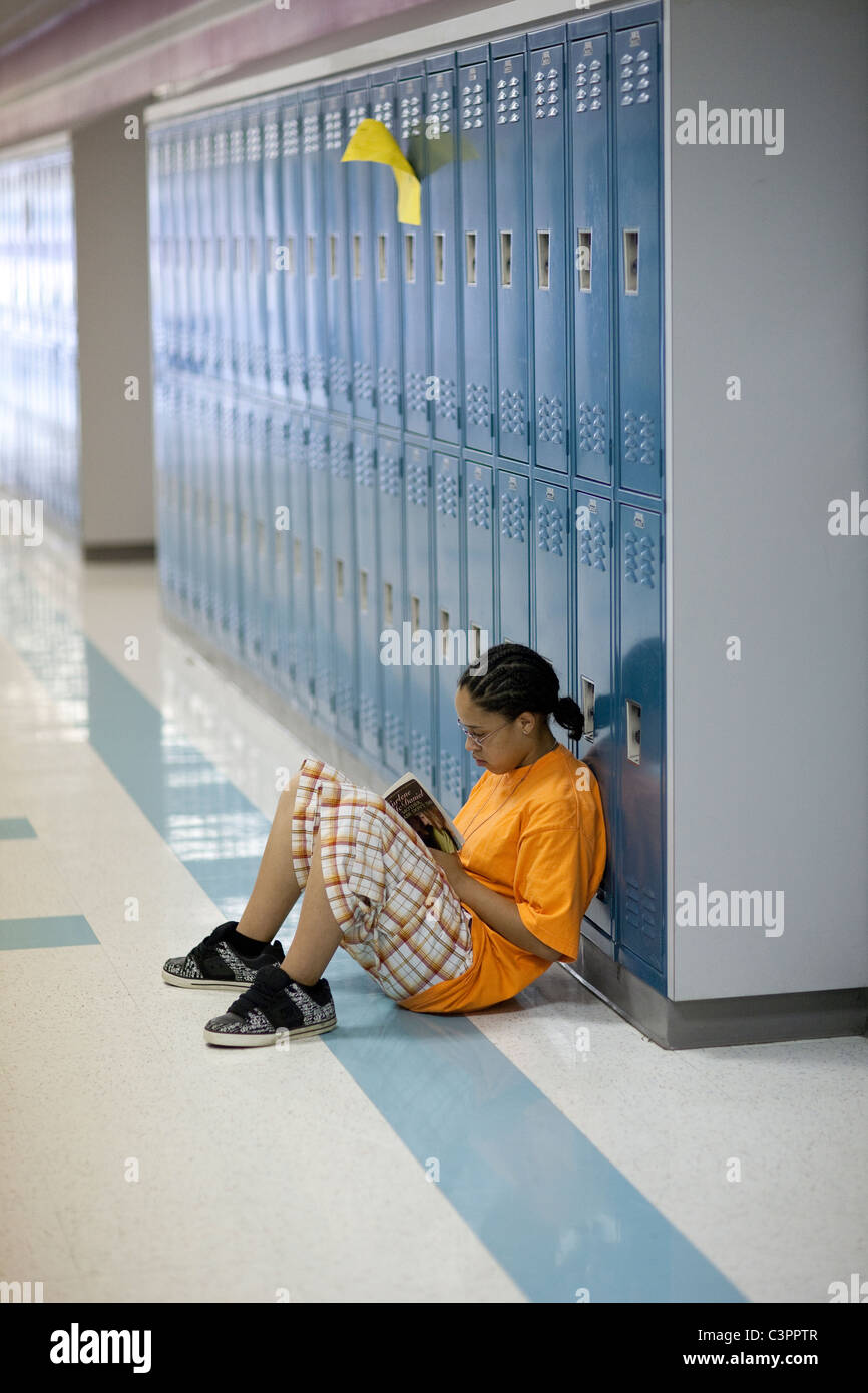 Young African-American teen male student reads alone while leaning against row of lockers in hallway of middle school in Texas Stock Photo
