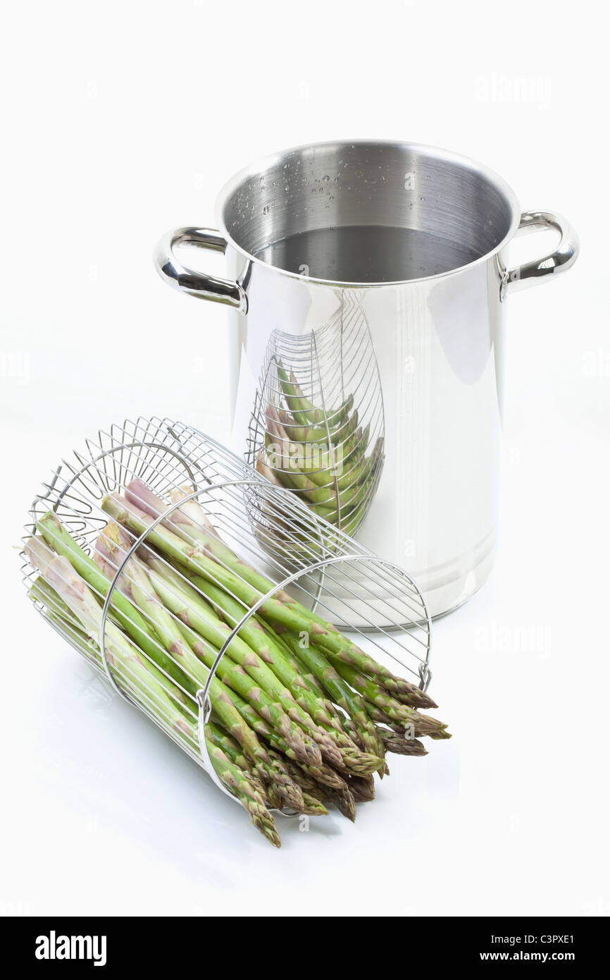 Asparagus in container with cooking pot on white background Stock Photo