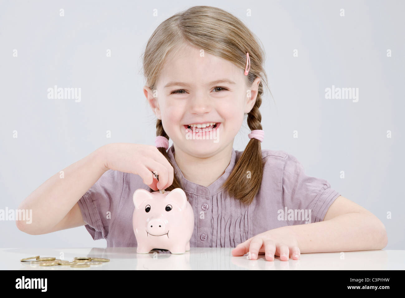 Girl (4-5) putting coin into piggy bank, smiling, portrait Stock Photo