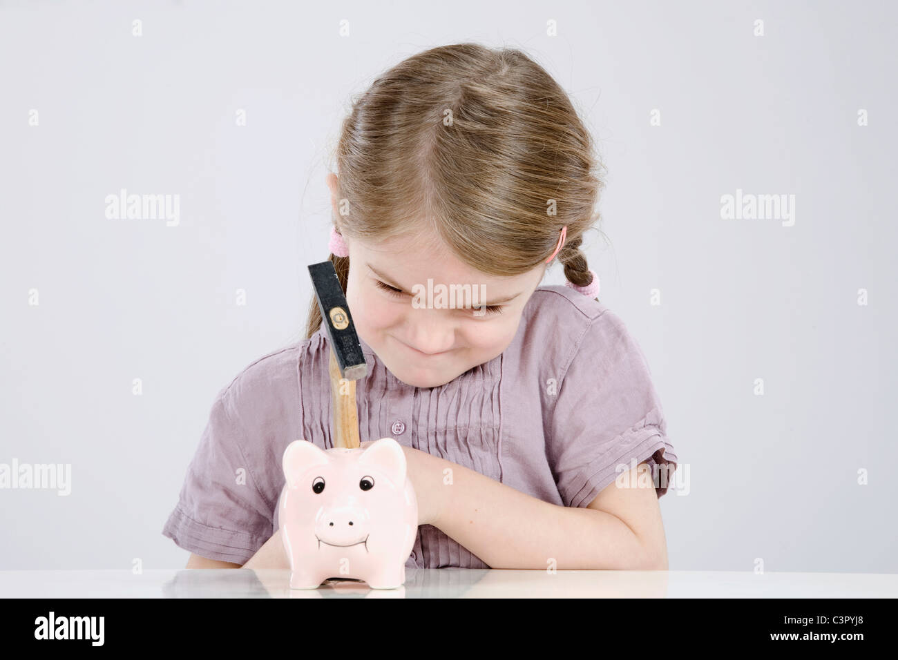 Girl (4-5) with a hammer is about to break a piggybank Stock Photo