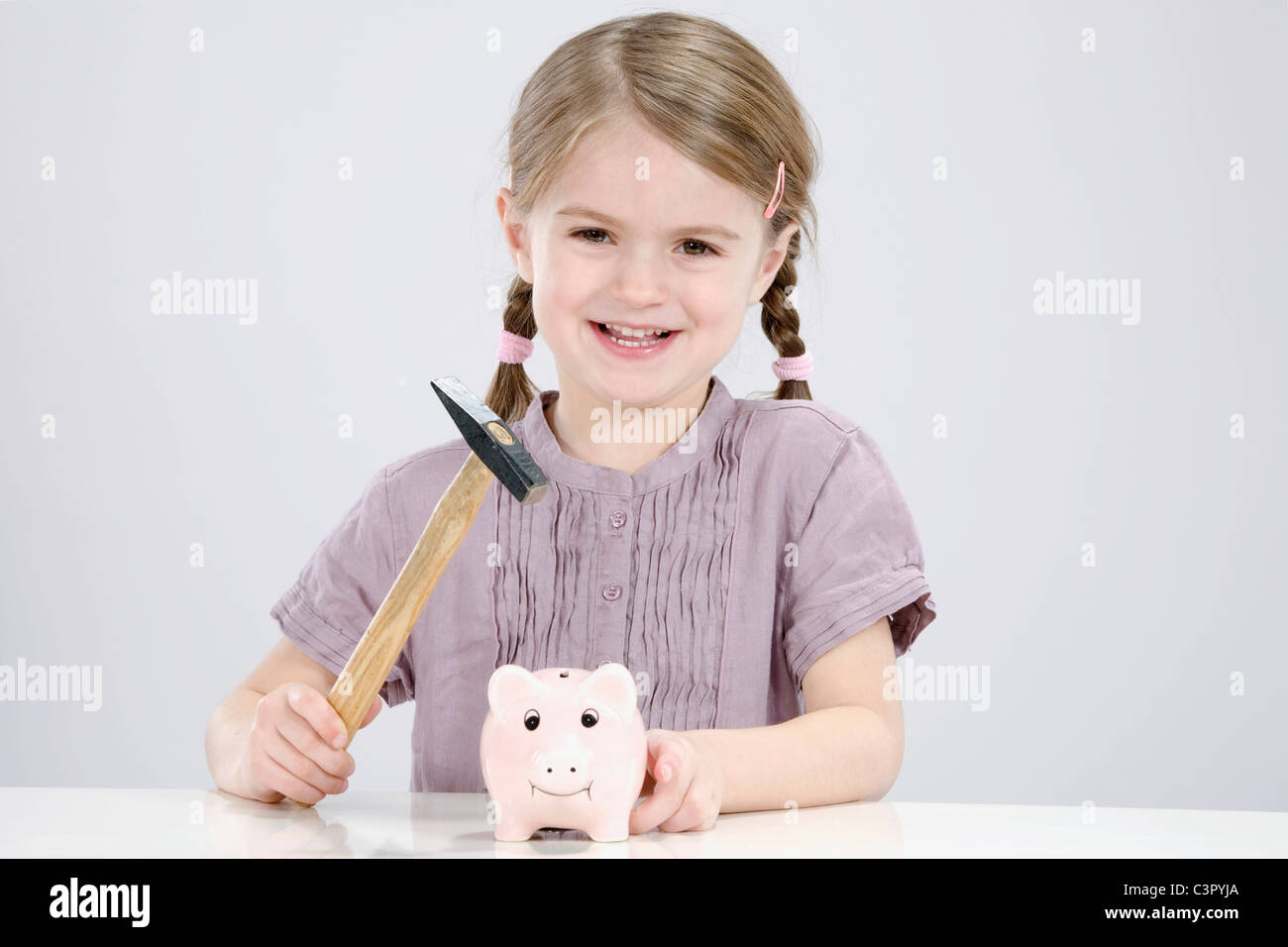 Girl (4-5) with a hammer is about to break a piggybank Stock Photo