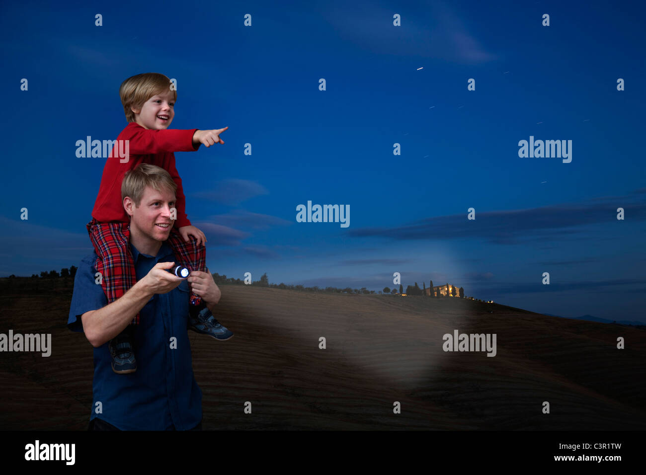 Italy, Tuscany, Father carrying son on shoulder with flashlight at night Stock Photo