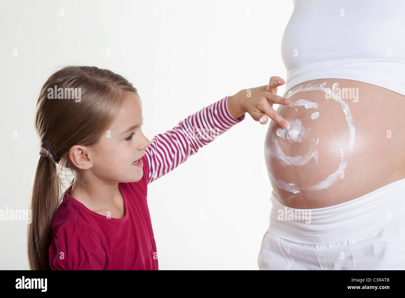 Daughter drawing smiley face on stomach of her pregnant mother Stock Photo