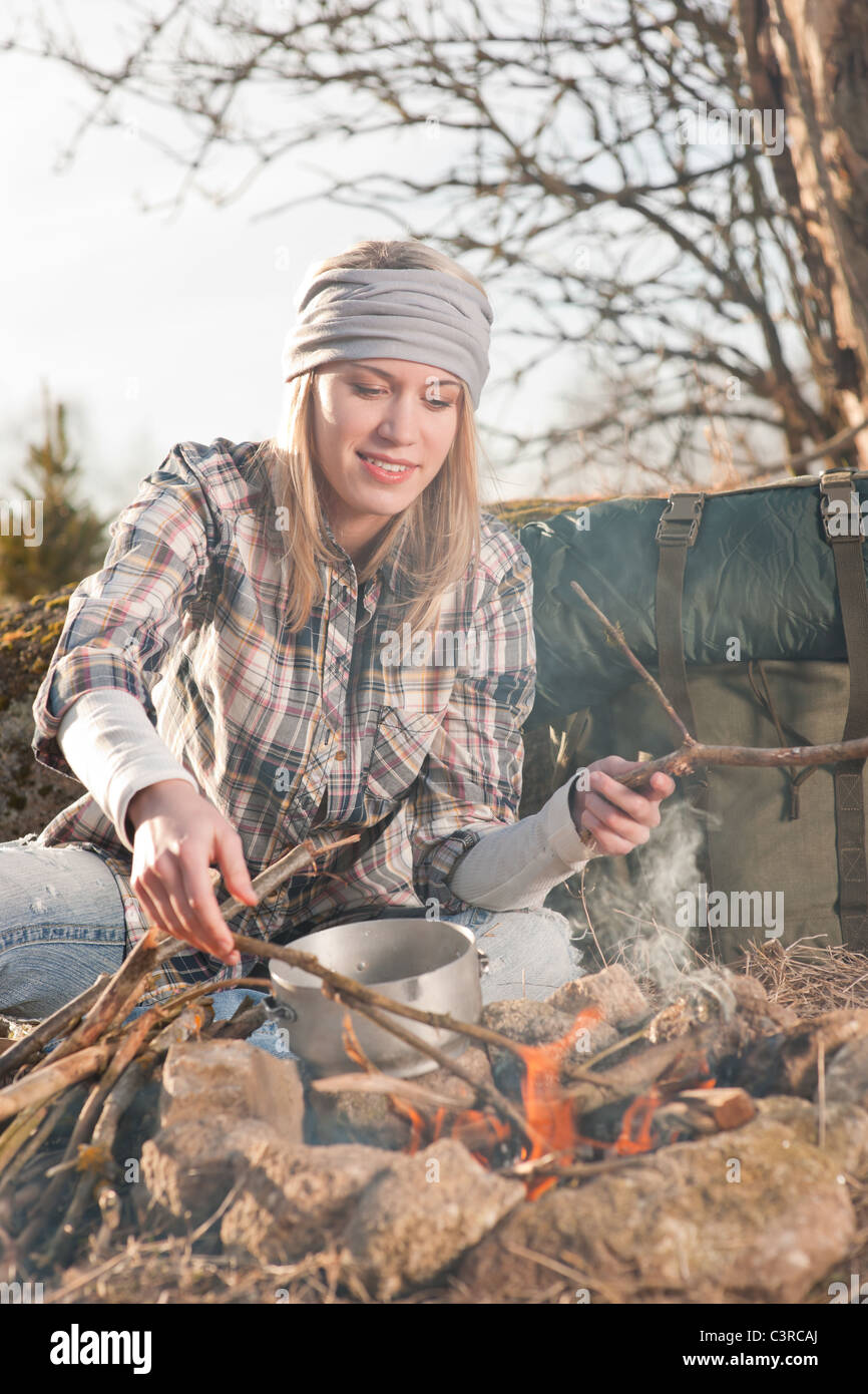 Young hiking woman with backpack cook on campfire in countryside Stock