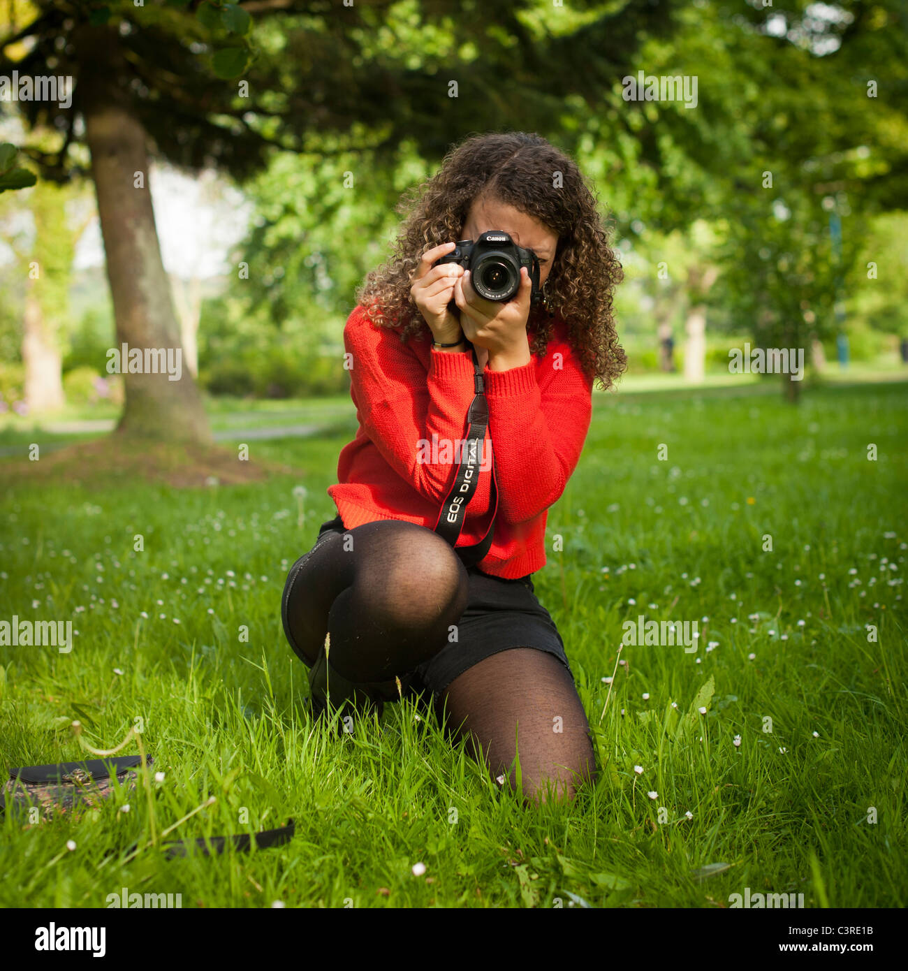 a 20 year old woman photographer wearing red jumper kneeling down taking a photo with a Canon ...